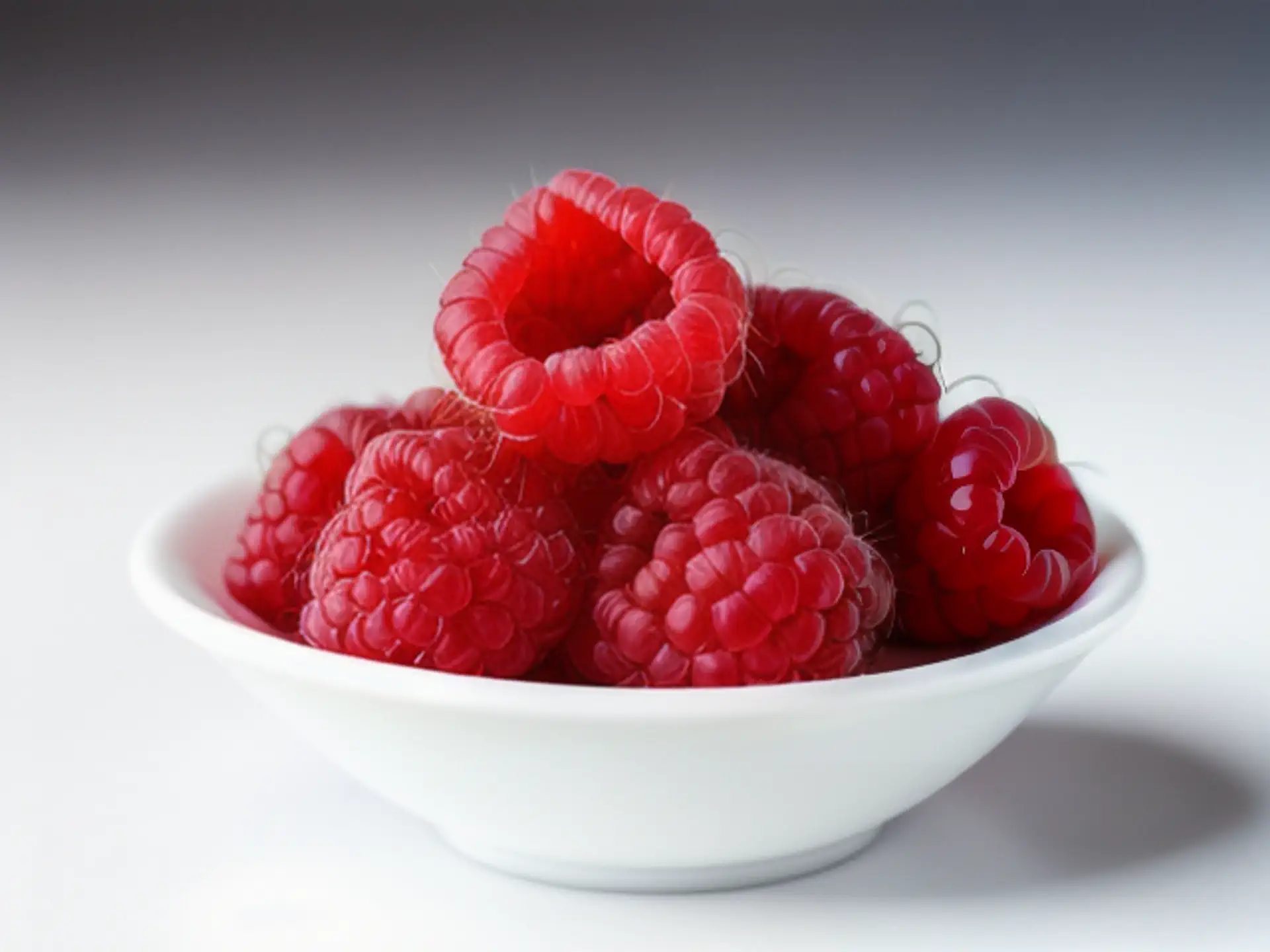 Verse rode frambozen in witte kom - close-up van sappig zomerfruit