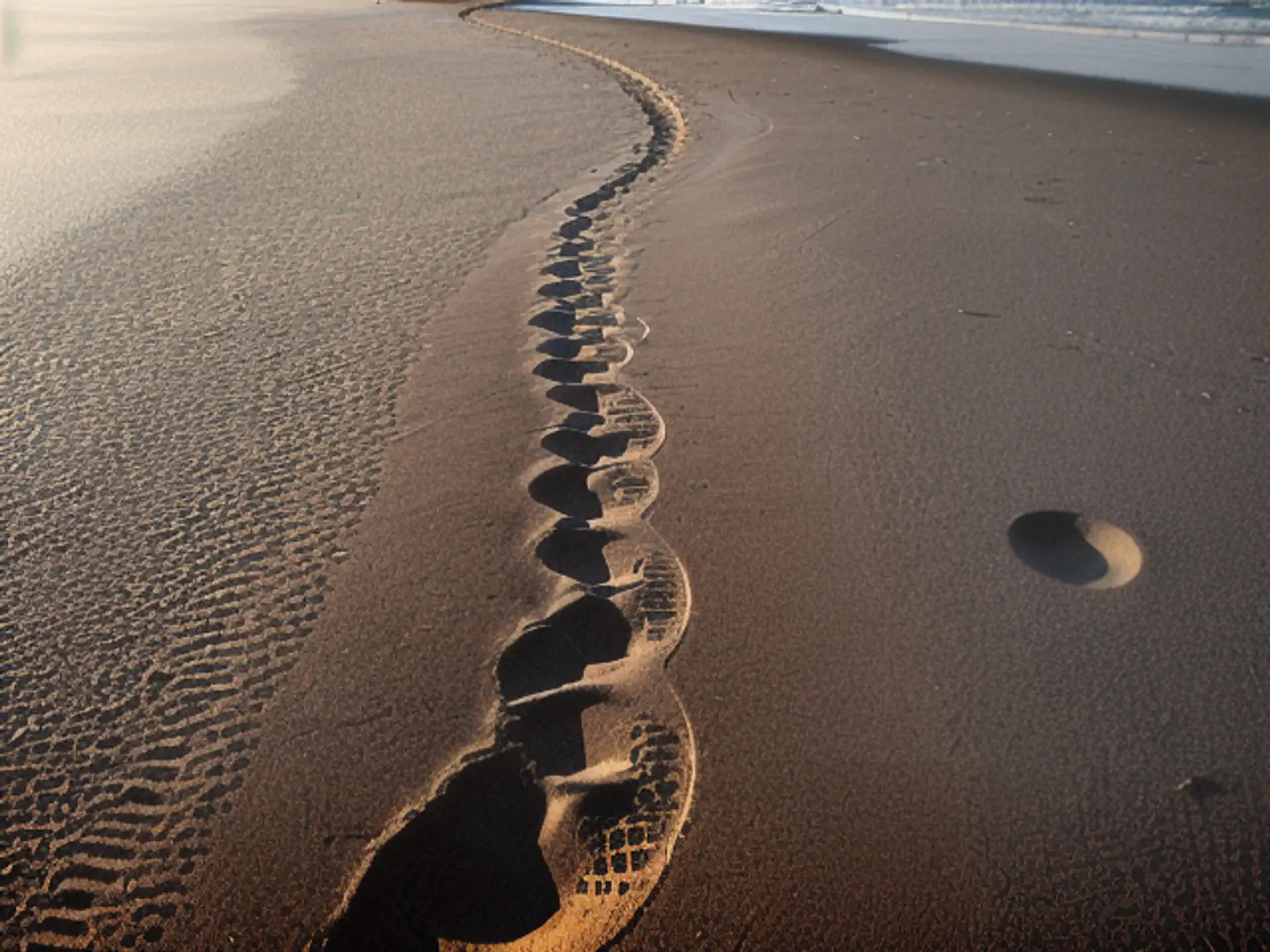 Slingerende voetstappen in nat zand tijdens gouden strandwandeling